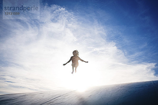 Glückliches Mädchen springt bei Sonnenschein auf Sportrampe gegen den Himmel