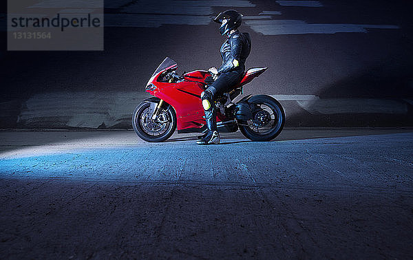 Seitenansicht eines Motorradfahrers  der auf einem Motorrad sitzt  auf der Straße an einer Mauer