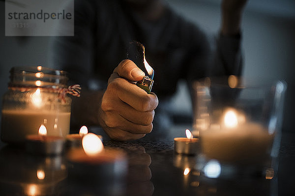 Mittelsektion eines Mannes  der Kerzen mit Zigarettenanzünder auf dem Tisch in der Dunkelkammer entzündet