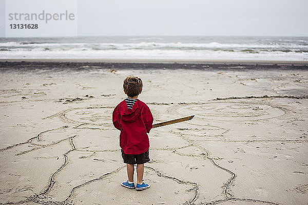 Rückansicht eines Jungen  der auf Sand am Strand steht