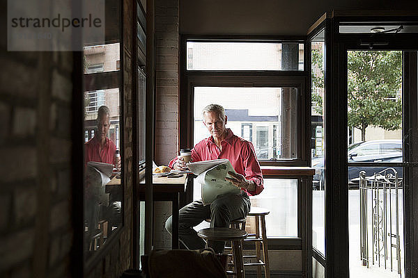 Reifer Mann liest Zeitung  während er Kaffee im Café trinkt