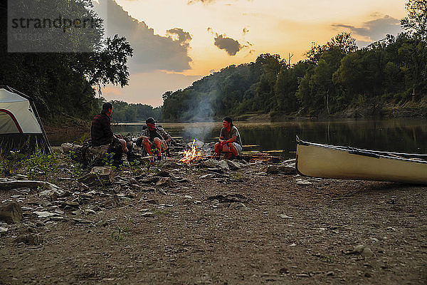 Freunde unterhalten sich  während sie bei Sonnenuntergang am Campingplatz gegen den Himmel sitzen