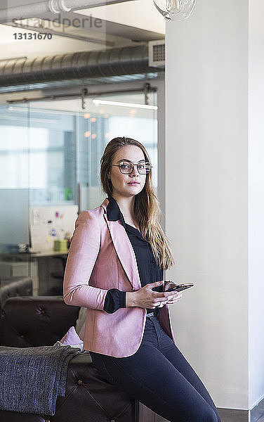 Porträt einer Frau  die ein Mobiltelefon benutzt  während ein Kollege im Büro Zeitung liest