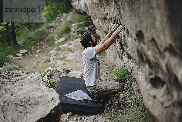 Mann kauert auf Bouldermatte  während er sich im Wald auf Felsklettern vorbereitet