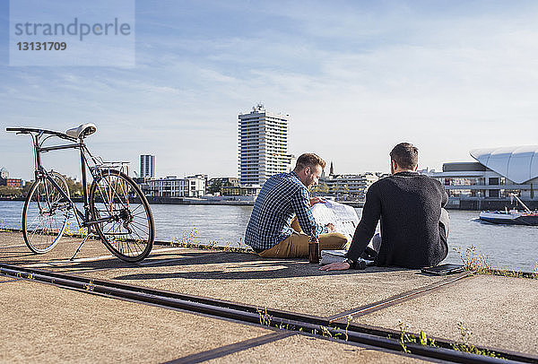 Freunde betrachten Dokument  während sie mit dem Fahrrad auf der Promenade gegen den klaren Himmel sitzen