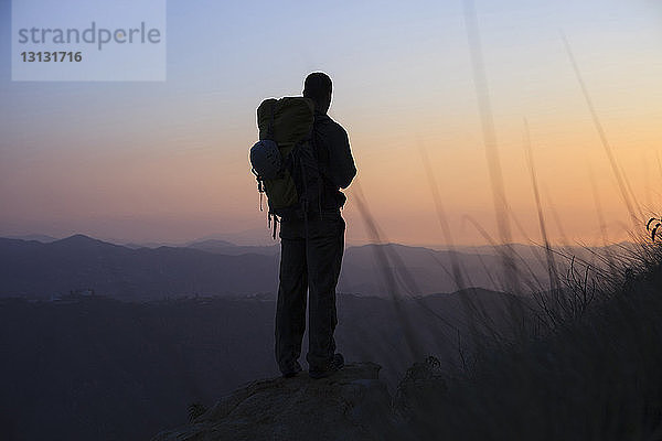 Scherenschnitt eines Mannes  der auf einem Felsen steht und bei Sonnenuntergang die Aussicht betrachtet
