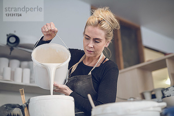 Niederwinkelansicht einer Frau  die in einem Workshop Farbe in einen Behälter gießt