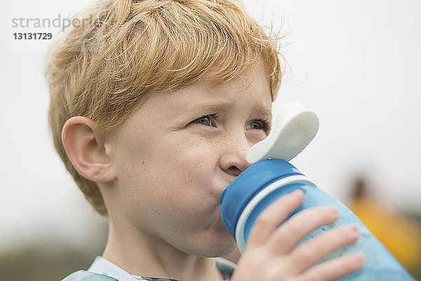 Nahaufnahme eines Jungen  der wegschaut  während er Wasser gegen den Himmel trinkt