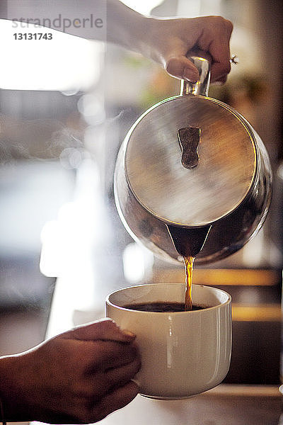 Ausgeschnittenes Bild eines Barista  der im Café Kaffee in eine Tasse gießt