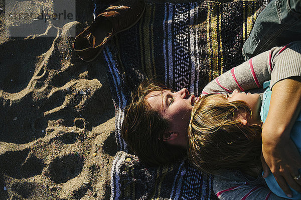 Draufsicht einer Frau  die ihre Tochter umarmt  während sie auf einem Strandtuch liegt