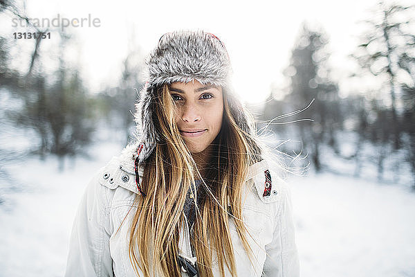 Porträt einer lächelnden Frau mit Pelzmütze auf schneebedecktem Feld