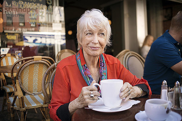 Nachdenkliche ältere Frau hält Kaffeetasse im Straßencafé
