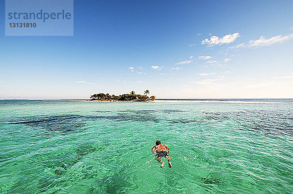 Rückansicht eines im Meer schwimmenden Menschen gegen den Himmel