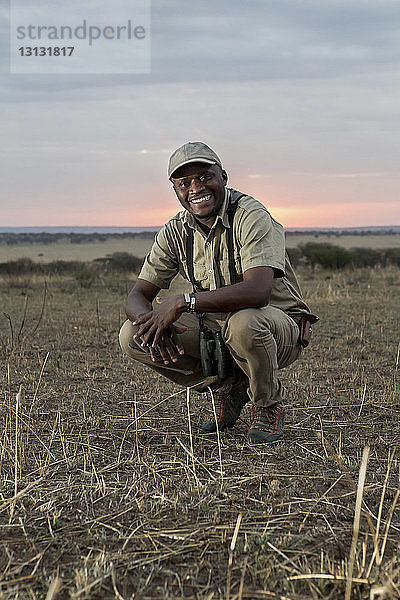 Porträt eines glücklichen Mannes  der auf einem Grasfeld im Serengeti-Nationalpark kauert