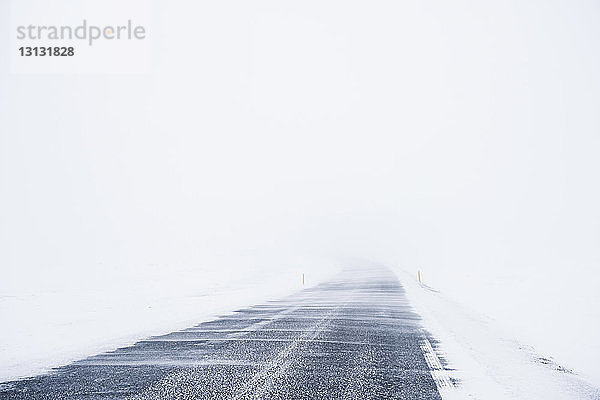 Leere Straße inmitten eines schneebedeckten Feldes vor klarem Himmel