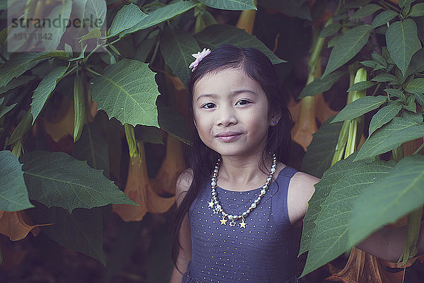 Porträt eines niedlichen Mädchens  das inmitten blühender Pflanzen im Park steht