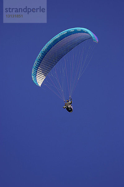 Tiefblick auf einen Mann beim Gleitschirmfliegen bei klarem blauen Himmel