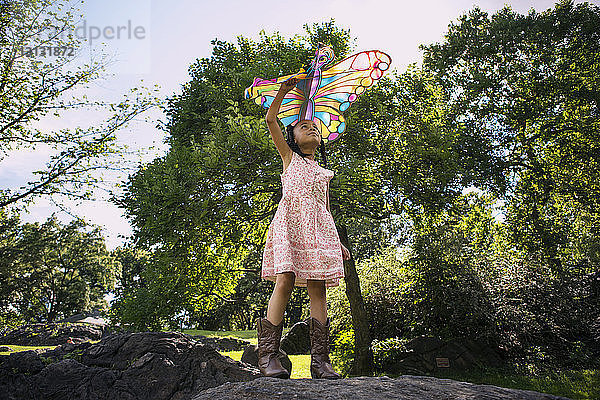 Niedrigwinkelansicht eines Mädchens  das einen Drachen hält und auf einem Felsen im Park steht