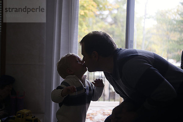 Vater und Sohn küssen sich  während sie zu Hause am Fenster stehen