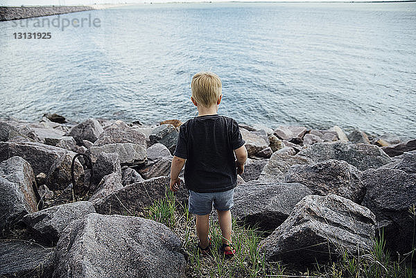 Rückansicht eines am Felsstrand stehenden Jungen