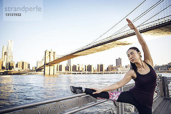 Athletin streckt Bein und Arm auf der Promenade mit der Brooklyn Bridge im Hintergrund
