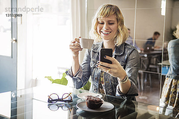 Glückliche Frau  die ein Smartphone benutzt  während sie im Cafe steht