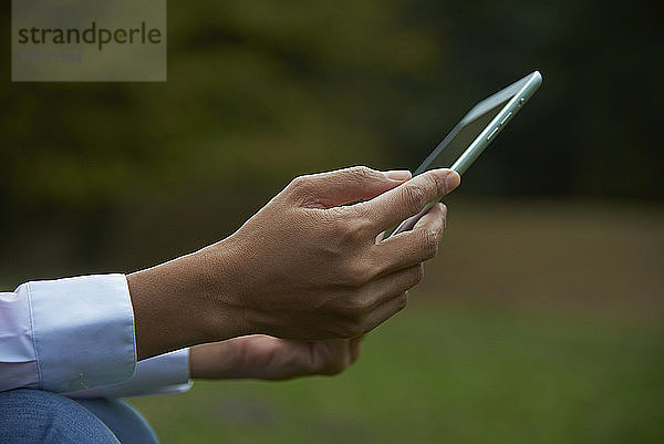 Abgetrennte Hände einer Geschäftsfrau  die einen Tablet-Computer im Park hält