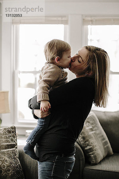 Mutter küsst Sohn  während sie ihn zu Hause im Wohnzimmer trägt