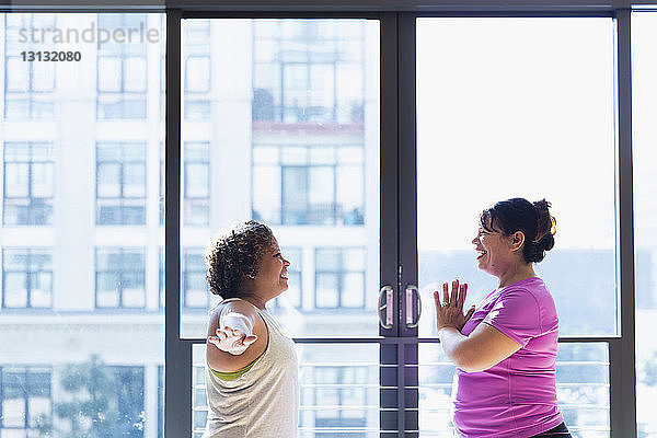 Glückliche Freunde üben von Angesicht zu Angesicht  während sie im Yoga-Studio am Fenster stehen