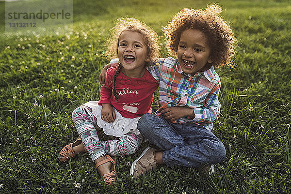 Fröhliche Geschwister sitzen auf einem Grasfeld im Park