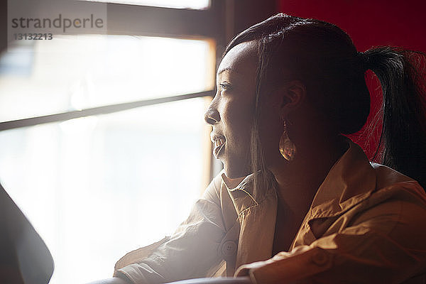 Seitenansicht einer jungen Frau  die an einem sonnigen Tag am Fenster sitzt