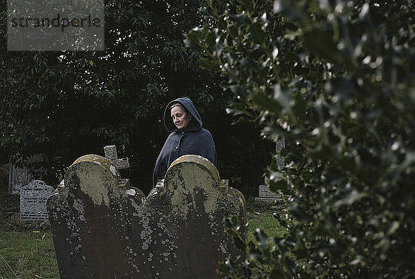 Traurige Frau mit Mantel auf dem Friedhof