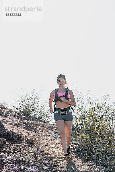 Weibliche Wanderin läuft bei Sonnenschein auf Berg gegen klaren Himmel