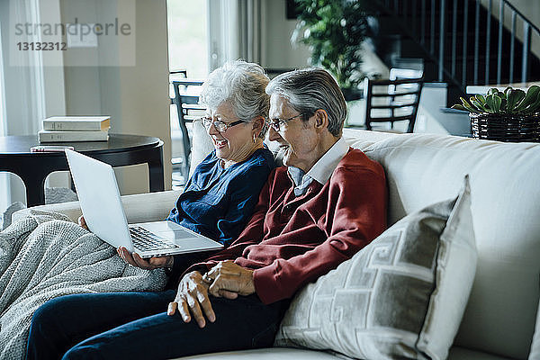Älteres Ehepaar bei Videokonferenzen über Laptop-Computer  während es auf dem Sofa sitzt
