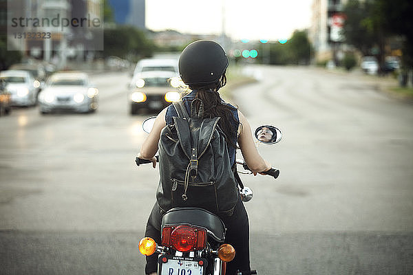 Rückansicht einer Frau mit Rucksack auf einem Motorrad auf der Straße