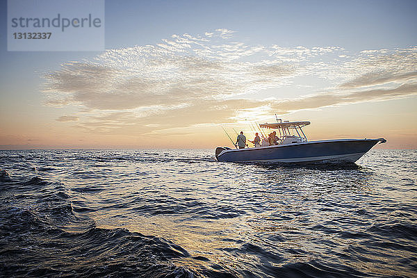 Freunde genießen auf dem Boot auf See gegen den Himmel bei Sonnenuntergang