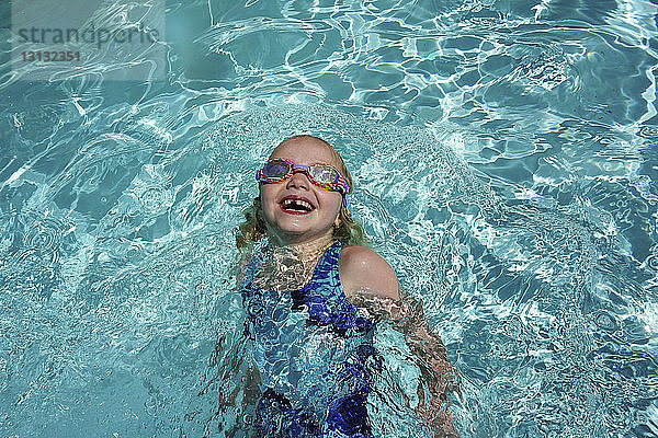 Hochwinkelansicht eines glücklichen Mädchens  das am sonnigen Tag im Pool eines Touristenortes schwimmt