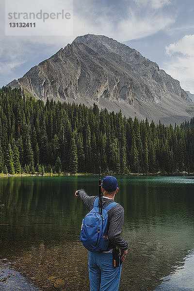 Rückansicht eines Wanderers mit Rucksack in Richtung See  während er im Wald vor den Bergen steht