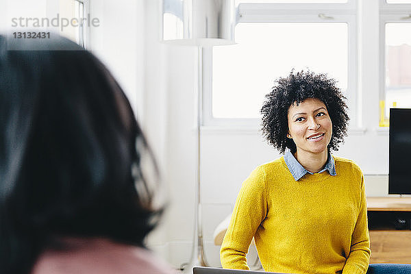 Lächelnde Geschäftsfrau im Gespräch mit einer Kollegin während der Arbeit im Büro