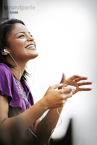 Lächelnde Frau mit Kopfhörer und Smartphone gegen den Himmel