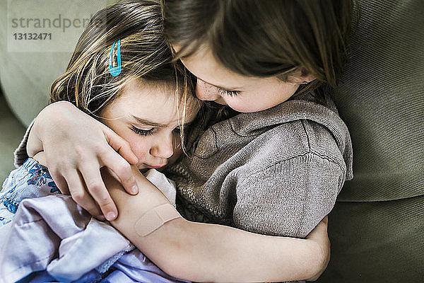 Hochwinkelansicht eines Mädchens  das seine Schwester umarmt  während es zu Hause auf dem Sofa sitzt