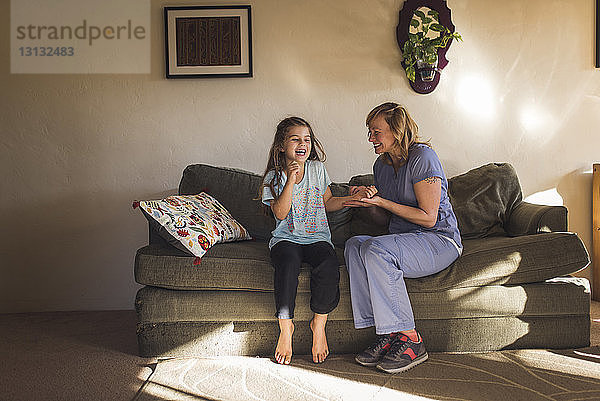 Glückliche Ärztin kontrolliert den Puls eines Mädchens  während sie zu Hause auf dem Sofa sitzt