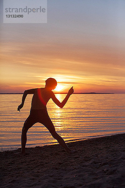 Silhouette eines Jungen  der am Strand einen Stein ins Wasser wirft