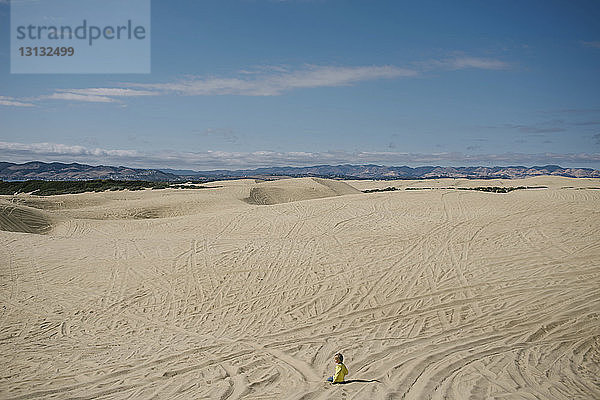 Hochwinkelansicht eines auf Sand knienden Mädchens gegen den Himmel