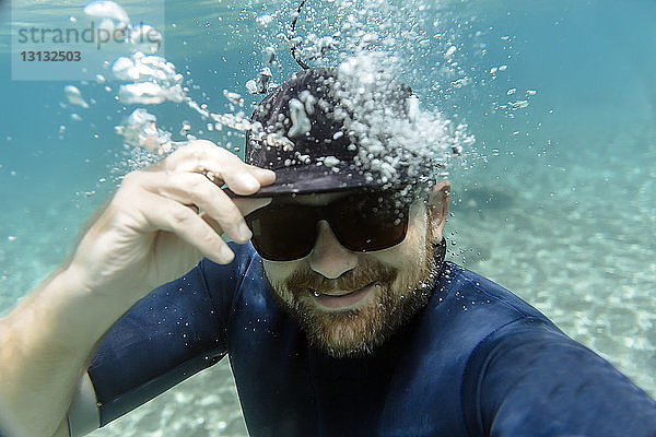Porträt eines glücklichen Mannes mit Sonnenbrille beim Unterwasserschwimmen