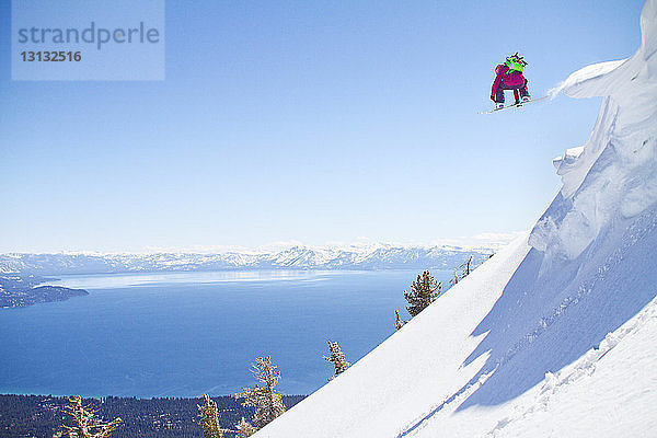 Snowboarder springt von schneebedecktem Berg gegen klaren Himmel