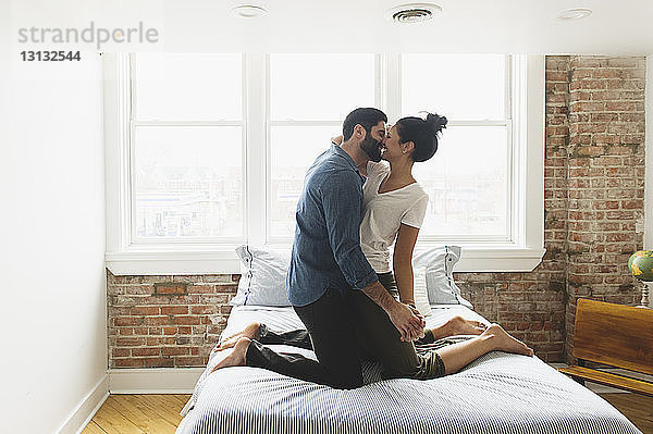 Romantisches Paar  das sich zu Hause kniend im Bett küsst