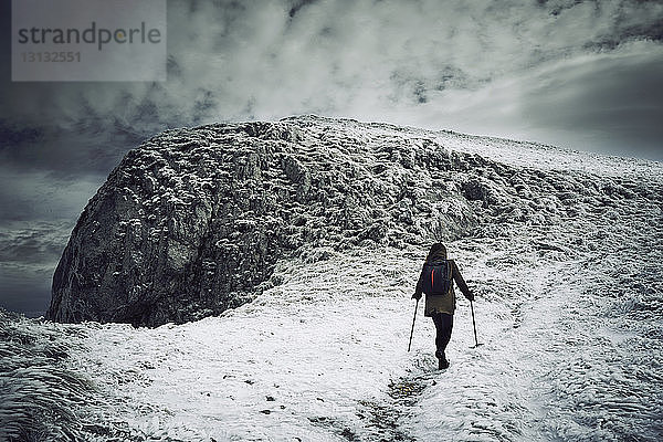 Rückansicht einer Wanderin  die auf einem schneebedeckten Berg vor bewölktem Himmel wandert