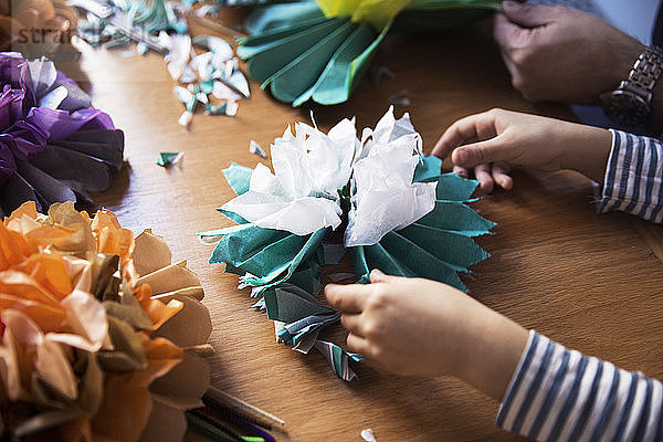 Beschnittenes Bild eines Mädchens und eines Vaters  die bei Tisch Papierblumen basteln