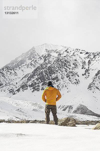 Rückansicht eines auf einem schneebedeckten Feld stehenden Mannes gegen den Himmel